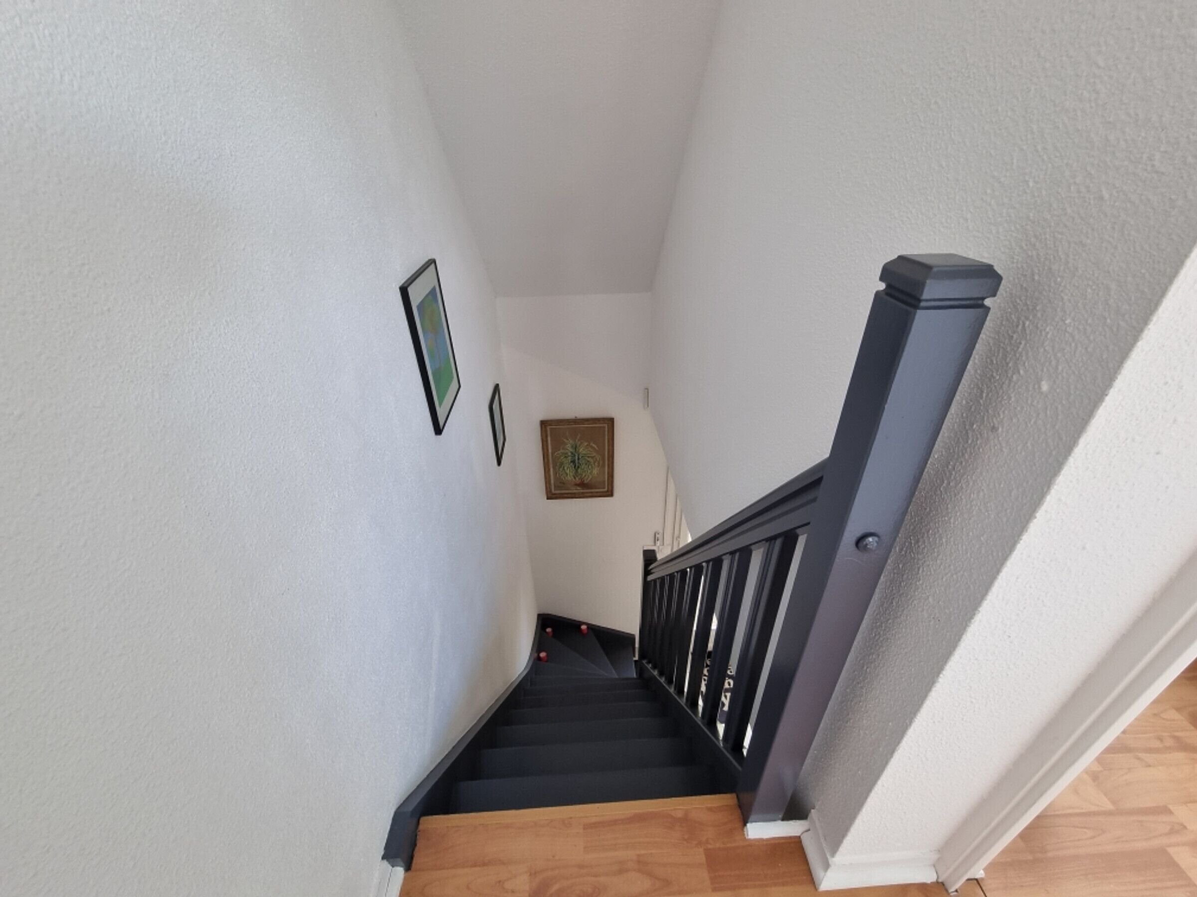Una escalera con barandilla de madera y pasamanos negro, que conduce a un rellano con cuadros en la pared.