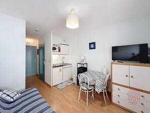 A compact living space with a kitchenette, a dining area with a table and chairs, a television, and a sofa. - Studio, pets allowed, balcony - 2 guests (Lamalou-les-Bains)
