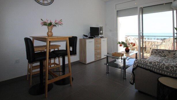 Ein modernes Wohnzimmer mit Essbereich, Fernseher, einer Uhr und einem Balkon mit Aussicht.