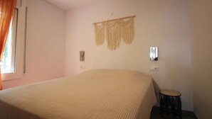 Ein Schlafzimmer mit einem großen Bett, einem kleinen runden Tisch, einer Wanddekoration aus Makramee und einem Fenster mit Vorhängen.