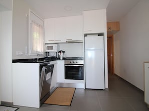 A compact kitchen with white cabinets, a microwave, a stove, and a refrigerator. - Renovated apartment sea view - guests (Llançà)