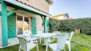 A patio with a table and chairs, a green door, and a hedge in the background. - Charming duplex near beach - 5 guests (Bias)