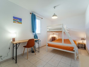 A bunk bed with an orange mattress, a desk with a chair, a lamp, and a painting on the wall.