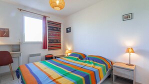A room with a bed, a desk, a chair, a lamp, and a window with a curtain. - Charming duplex near beach - 5 guests (Bias)