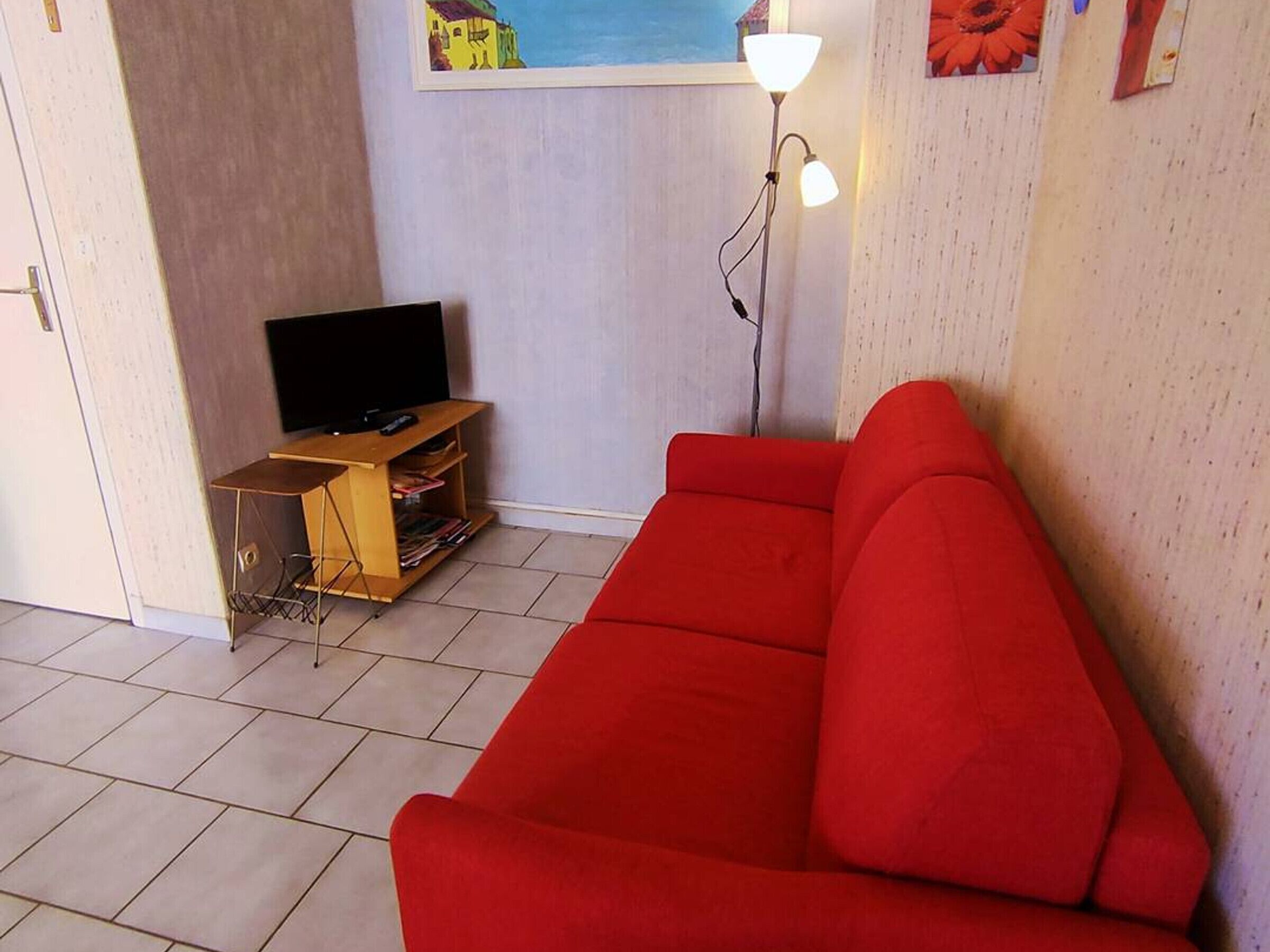 A living room with a red sofa, a TV on a wooden stand, and a floor lamp.
