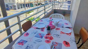 A balcony with a table set for dining, overlooking a street with buildings and palm trees. - Lovely apartment with panoramic view - 6 guests (Canet-en-Roussillon)