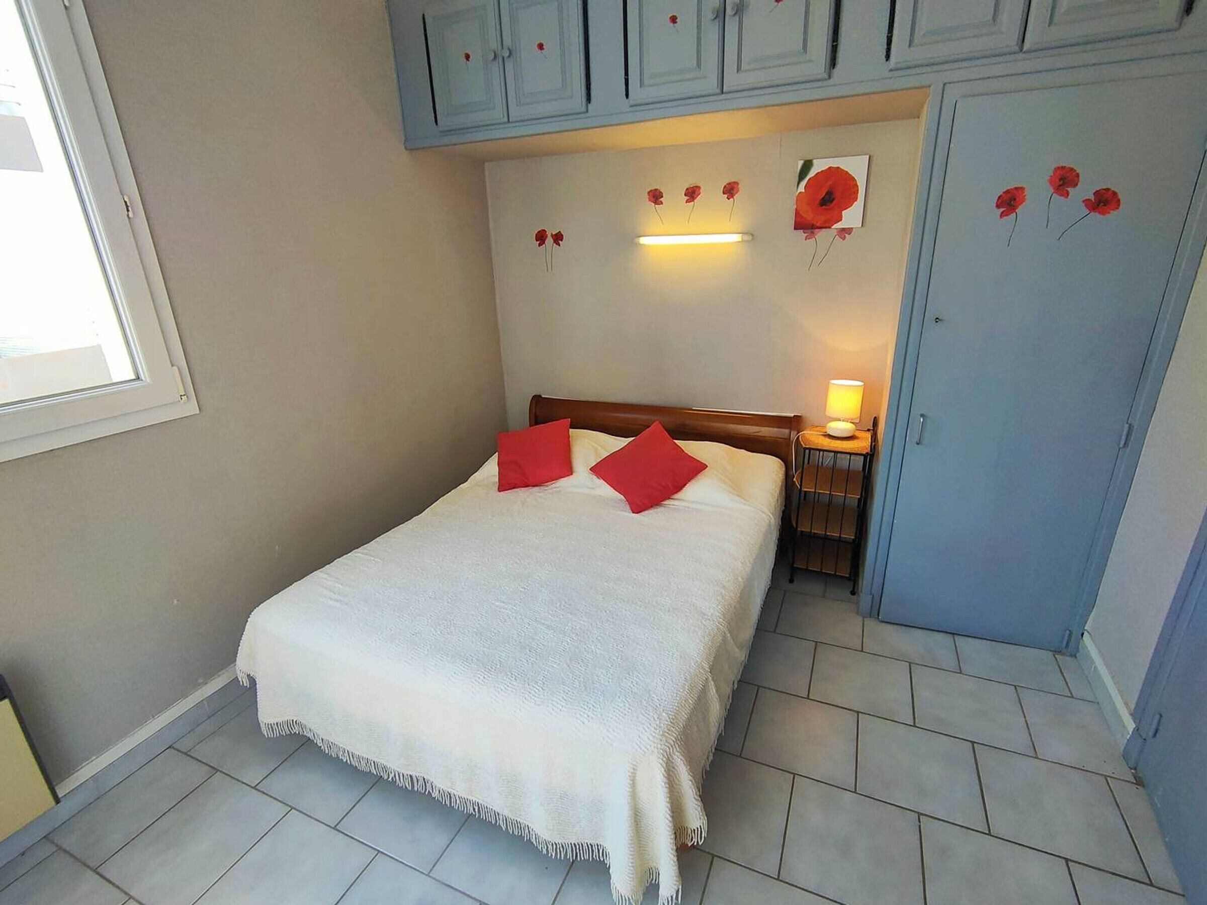 Een slaapkamer met een bed, nachtkastje, lamp en een garderobe.