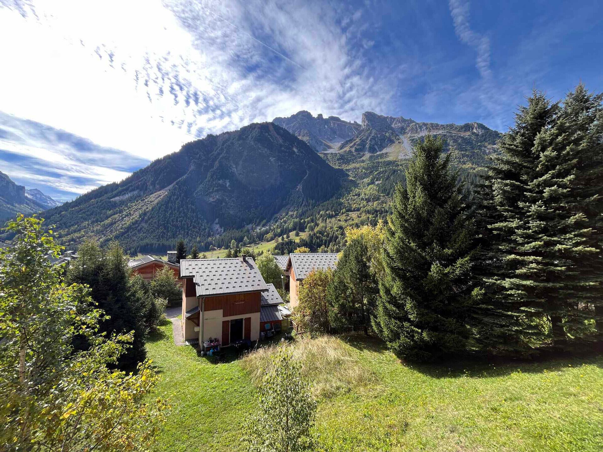 Un refugio de montaña con techo inclinado, rodeado de un bosque denso y una montaña destacada al fondo.
