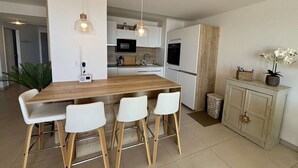 Una cocina moderna con una isla de madera, taburetes de bar blancos, luces colgantes y un horno empotrado.