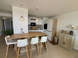 A modern kitchen with a wooden island, white bar stools, pendant lights, and a built-in oven. - Bright apartment, beach view - 5 guests (Port-la-Nouvelle)