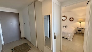 Una habitación de hotel con cama, mesita de noche, lámpara, espejo y puerta que da a otra habitación.