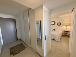 A hotel room with a bed, a bedside table, a lamp, a mirror, and a door leading to another room. - Bright apartment, beach view - 5 guests (Port-la-Nouvelle)
