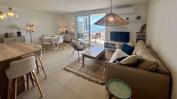 Una sala moderna con sofá, televisor, comedor y un balcón con vistas.