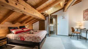Ein Schlafzimmer mit Holzboden, einem Bett mit Blumenmuster-Bettwäsche, einem Schreibtisch mit Stuhl und einem an der Wand befestigten Dekorationsobjekt – einem Hirschkopf.