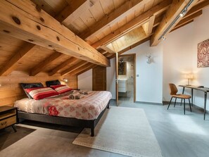 Een slaapkamer met een houten plafond, een bed met bloemenbedrukking, een bureau met stoel, en een decoratieve geweivleugel aan de muur.