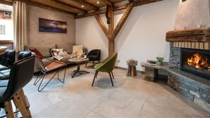 Ein Zimmer mit Kamin aus Stein, Holzbalkendecke, einem grünen Sessel und einer Couch.