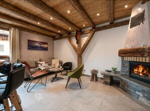 A room with a stone fireplace, wooden ceiling beams, a green chair, and a sofa. - Spacious house in La Plagne - 12 guests (La Plagne Montalbert)