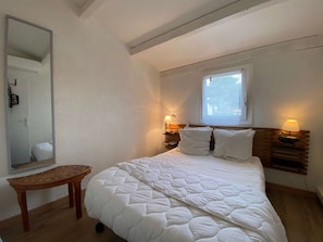 Ein Schlafzimmer mit einem Bett, Nachttischlampen, einem Fenster, einem Spiegel und einer hölzernen Bank.