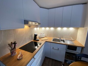 Eine moderne Küche mit einem schwarzen Induktionskochfeld, einem Toaster, einer Spüle und einer Mikrowelle.