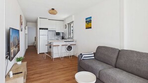 Eine moderne Wohnung mit grauem Sofa, Holzboden, einer Küche mit weißen Schränken und einem kleinen Essbereich.