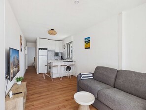 Eine moderne Wohnung mit grauem Sofa, Holzboden, einer Küche mit weißen Schränken und einem kleinen Essbereich.