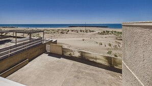 Blick auf einen Strand von einem Balkon mit blauem Himmel, Sandstrand und einem Felsenmole.