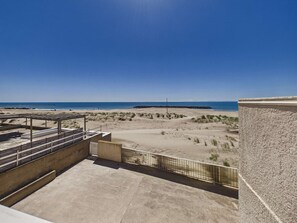 Blick auf einen Strand von einem Balkon mit blauem Himmel, Sandstrand und einem Felsenmole.