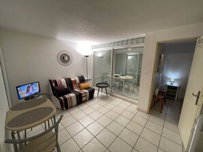 Ein Wohnbereich mit einer Couch, einem Fernseher, einem kleinen Tisch und einem Esstisch mit Stühlen.