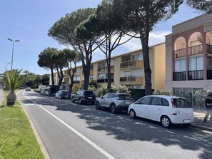 Eine Straße mit parkenden Autos und Bäumen, im Hintergrund mehrstöckige Gebäude.