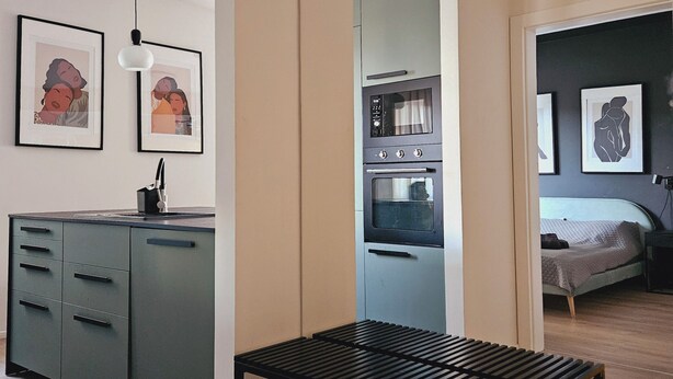 A modern kitchen with a built-in oven and a dining area with a black table. - Garbary Residence II Old Town (Poznań)