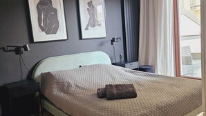 A bedroom with a bed, a bedside table, a lamp, two framed artworks, a window with curtains, and a view of the outside. - Garbary Residence II Old Town (Poznań)