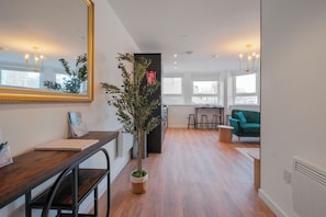 A modern interior with a wooden desk, a potted plant, a mirror, and a dining area with a green sofa. - City Point Aberdeen by Guestz (Aberdeen)