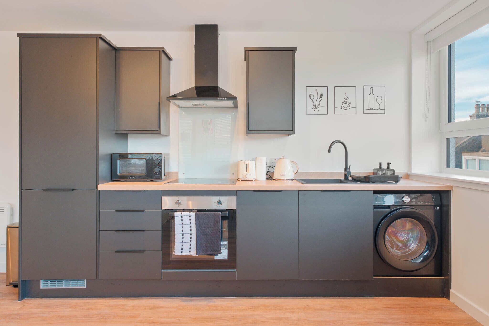 A compact kitchen with built-in appliances, a washing machine, and a window for natural light.