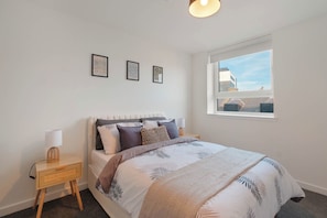 A bedroom with a bed, a nightstand, a lamp, and a window with a view. - City Point Aberdeen by Guestz (Aberdeen)
