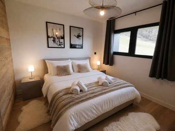 Ein Schlafzimmer mit einem Bett, zwei Nachttischen, einem Fenster mit Vorhängen und zwei gerahmten Bildern an der Wand.