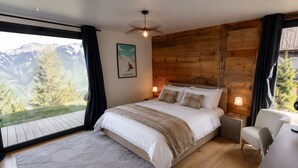 Un dormitorio con una cama grande, paredes de madera, vistas a montañas y un escritorio con una silla.