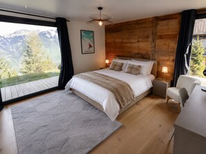 Ein Schlafzimmer mit einem großen Bett, Holzwänden, Bergblick und einem Schreibtisch mit Stuhl.