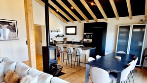 Una sala de estar moderna con sofá, mesa de comedor y sillas, una zona de cocina con estufa y un amplio ventanal.