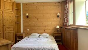 Ett sovrum med en sänggavel i trä, en säng med mönstrat sänglinne, två sänglampor och ett fönster med gardiner.