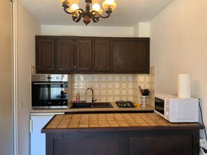 Eine Küche mit dunklen Holzausziehtüren, einem Edelstahlbackofen, einer Mikrowelle und einer gefliesten Spritzschutzwand.