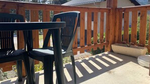 Um deck de madeira com mesa e cadeiras, um vaso de concreto e vista para uma montanha.