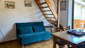 Um quarto com escada de madeira, sofá verde-azulado, mesa de madeira e duas molduras na parede.