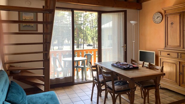 Quarto com teto de madeira, mesa de jantar com cadeiras, sofá, armário e porta de vidro deslizante para área externa com cadeiras.