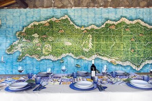 Una mesa de comedor dispuesta con platos, vasos y una botella, con un gran mural de un mapa al fondo.
