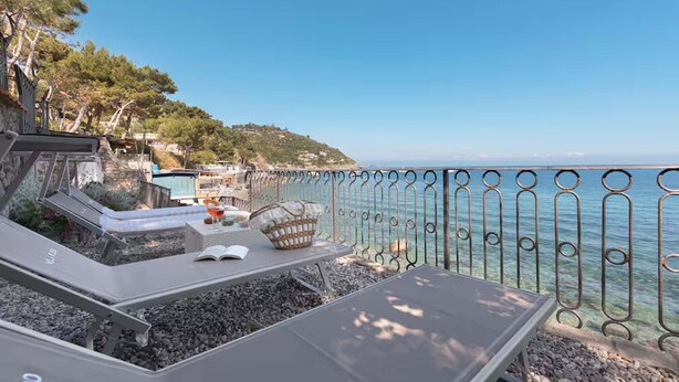 Una terrazza sul mare con poltrone, un tavolo e un parapetto metallico che si affaccia sul mare.