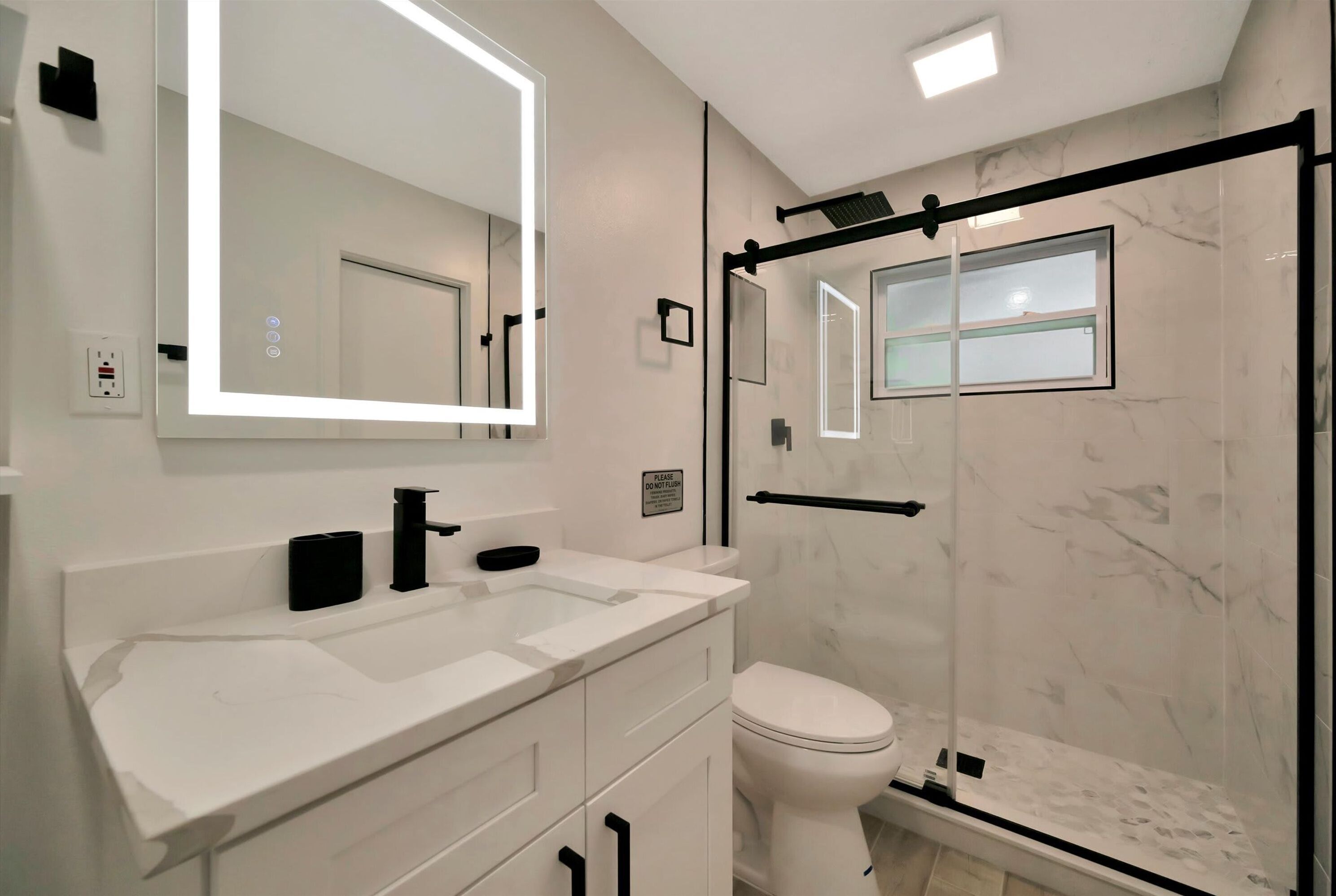 A modern bathroom with a white sink, a large mirror, a toilet, and a glass shower enclosure.