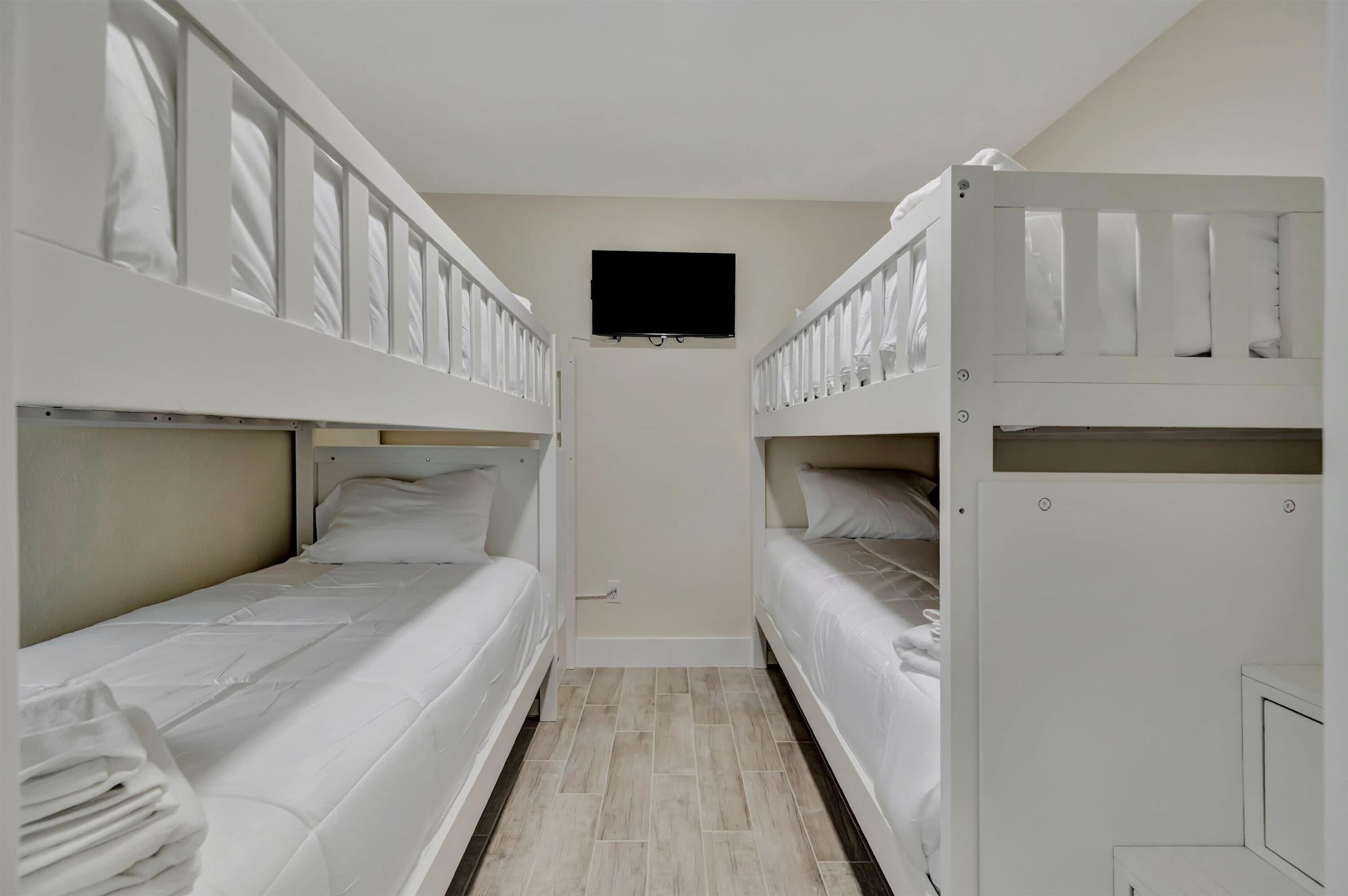 Una habitación de hotel con dos literas, una cama plana, un televisor montado en la pared y una puerta con manija.