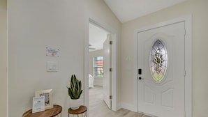 Un couloir avec une porte blanche, un panneau d’accueil, une plante en pot et une petite table.