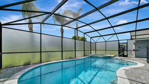 Une piscine intérieure avec des parois en verre transparent, une terrasse carrelée et un palmier à l’extérieur.