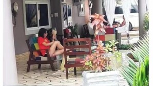 Un'area relax all'aperto coperta, con panche, sedie, una pianta in vaso e una finestra con tende.